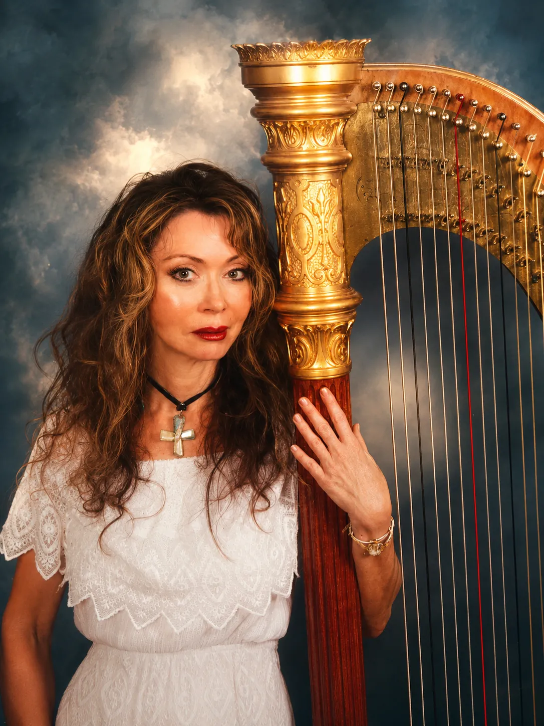 Dr. Marsha Long leaning against her golden concert pedal harp in a studio portrait