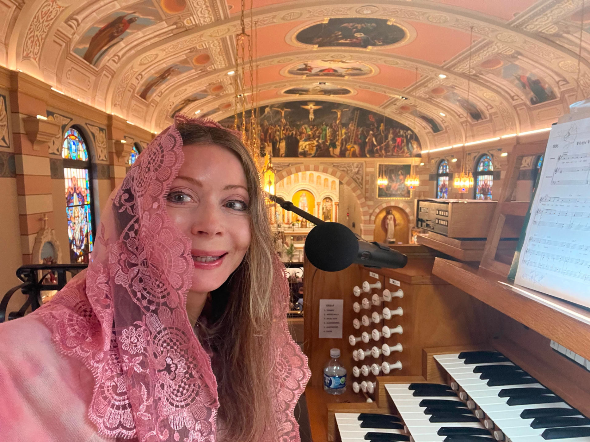 Dr. Marsha Long in a pink lace mantilla at the organ console of St. Mary's Catholic Church in Escondido, beneath the painted barrel-vaulted ceiling