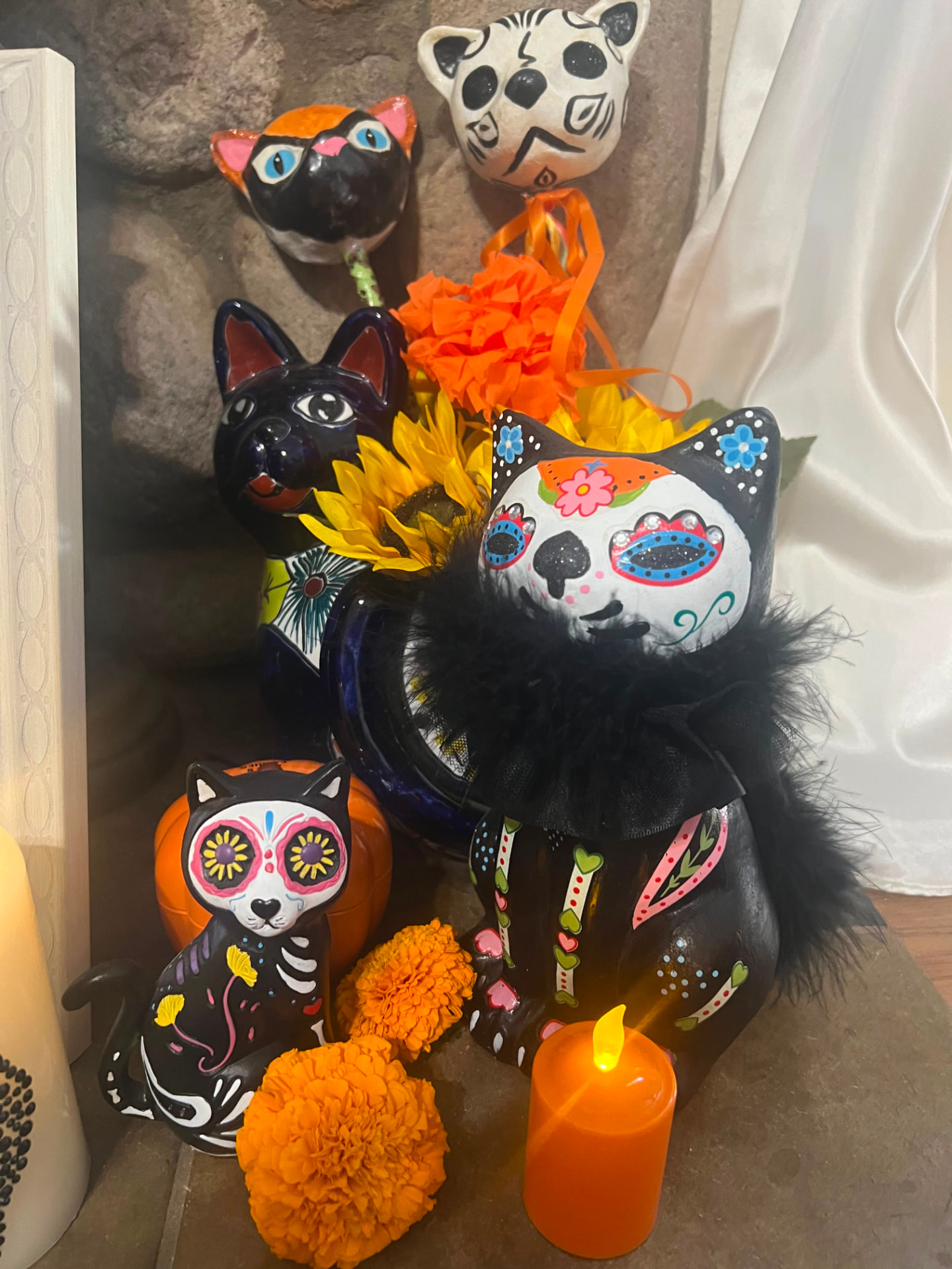 Hand-painted Día de los Muertos cat figurines with marigolds, sunflowers and a candle on a home altar