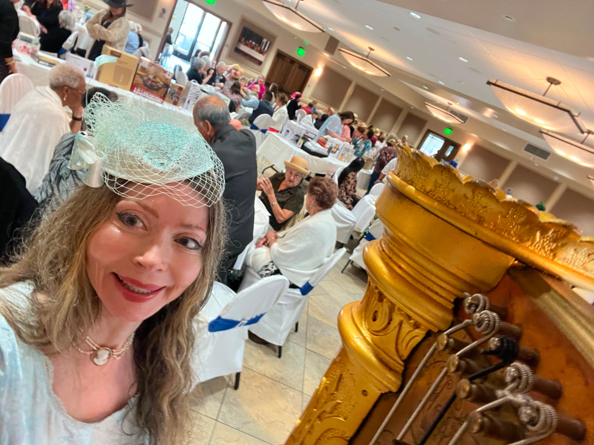 Dr. Marsha Long in a mint vintage hat and veil beside her gilded pedal harp at a costume tea recital