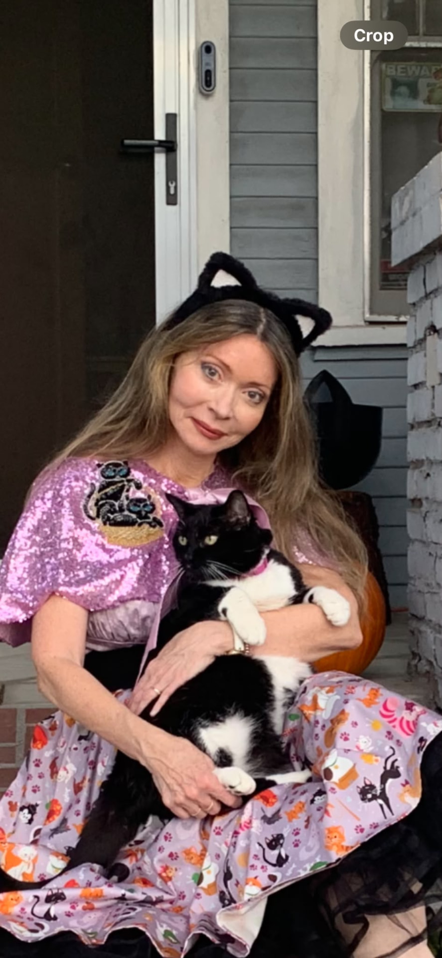 Dr. Marsha Long in a cat-themed costume recital gown, holding her tuxedo cat on a front porch