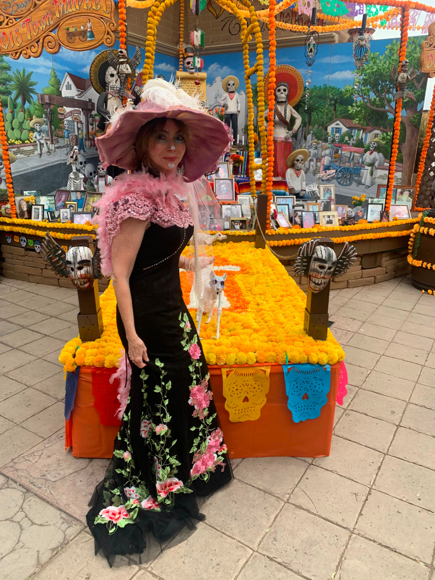 Dr. Marsha Long as La Catrina in a black rose gown and pink plumed hat before the Old Town San Diego Día de los Muertos ofrenda